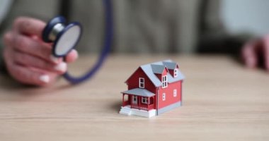 Kadın, steteskopu oyuncak evine satılık olarak koyar. Durumu kontrol etmek için ahşap masanın üzerinde durur. Sigortanın yavaş çekim sağlanmasında teşhis ve ev bakımı kavramı