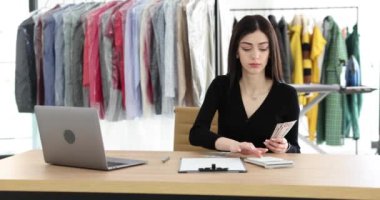 Odaklanmış çalışanlar, çamaşırhanede askı başında oturarak para kazanıyorlar. Kadın işçi hesaplanmış nakit miktarını iş yerindeki defterine yazıyor. Kuru temizleme yapıyorum.