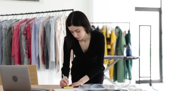 女性マネージャーは黄色のシートシールに所有者データを書き込み 服に添付します 洗濯室で働く女性 スローモーション — ストック動画