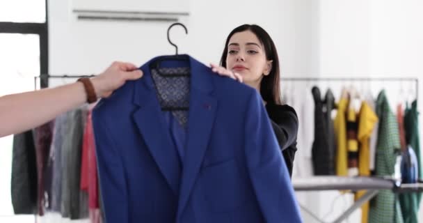 女性のブルネットのマネージャーはクリーンアップのためにクライアントから青いジャケットを取ります 女性従業員は ドライクリーニングサービスの高品質を提供しますスローモーション — ストック動画