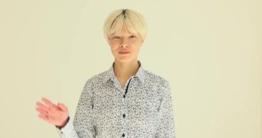 Sarışın kadın selamlaşmak için el sallıyor ve güzelce gülümsüyor. Ofisteki kadın, ağır çekimde hafif duvara karşı duran ziyaretçiye merhaba diyor.