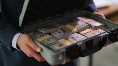 Takım elbiseli bir işadamı para dolu bir bavulu yakın planda tutuyor. Kârlı finansal anlaşmalar kavramı