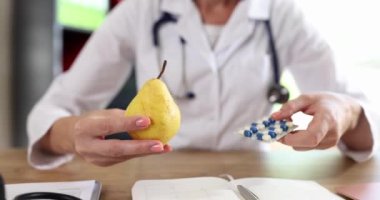 Kadın doktor klinikteki masada taze armut ve el hapları sunuyor. Profesyonel beslenme uzmanı taze meyve ve diyet takviyeleri tavsiye ediyor