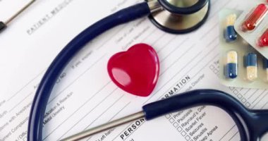 Kırmızı kalp oyuncağı ve steteskop hasta tıbbi geçmişi formunda hapların yanında yatıyor. Klinikte kalp hastalıkları tedavisi için tıbbi ekipman ve ilaçlar