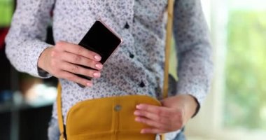 Bayan çalışan akıllı telefonu hardal rengi deri çantaya koyup işten sonra eve gitmeye hazır hale getiriyor. Kadın parlak pencerenin yanında duruyor ağır çekimde