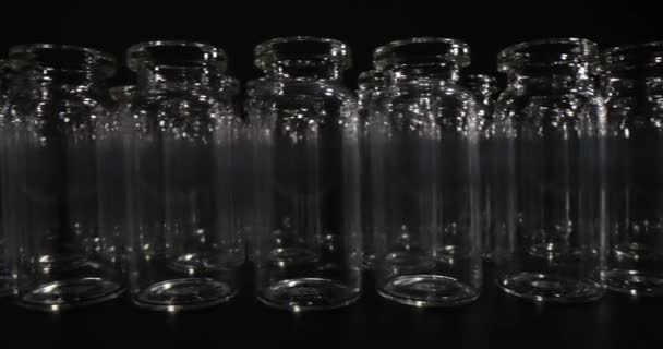 暗いテーブルの上に長い列に立ってワクチンのための透明なガラスのバイアル 黒を背景にした実験室や医療用ガラス — ストック動画