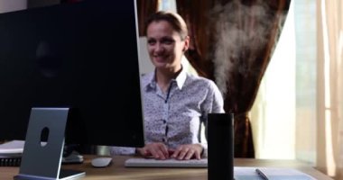 Ofiste çalışan hava nemlendiricisinin yanındaki bilgisayar klavyesinde gülümseyen kadın tipleri. İş yerinde Aromaterapi ve ferahlatıcı aygıt