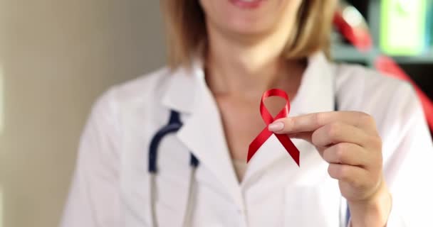 白衣を着た女医はエイズと戦う赤いリボンのシンボルを持っていて 笑顔を上げています Hivの認識と疾患の概念の予防 — ストック動画