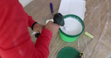 İnşaatçı, yenilenmiş düz çekimde endüstriyel karıştırıcıyla kovada boya karıştırıyor. Ressam işyerinde inşaat malzemesi hazırlıyor.