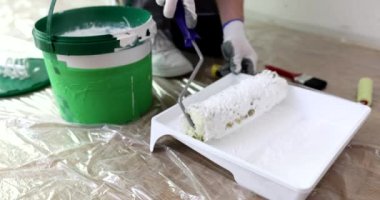 Ressam ağır çekimde tepsiden beyaz boya ve tekerlekli fırça alır. İşçi muhafaza onarımı sırasında araç üzerine renk pigmenti uygular