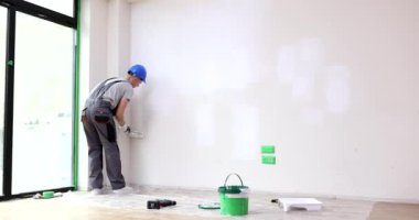 Miğferli bir miğfer, geniş ofis ağır çekimde duvarları tekerlekli fırçayla boyuyor. Tamirci, muhafaza yenileme sırasında beyaz renk uygular