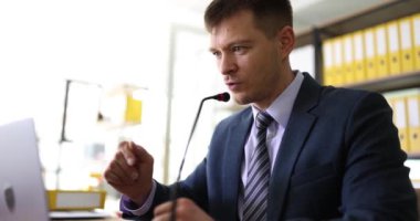 Mikrofonlu bir iş adamı, iş arkadaşlarıyla ağır çekimde görüntülü konuşma yapar. Yönetici çevrimiçi konferansa dizüstü bilgisayarla katılıyor