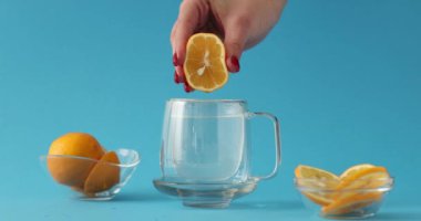 Mavi arka planda cam bardakta suya damlayan taze limon sıkan bir kadın eli. Sabah ağır çekimde narenciye içeren sağlıklı bir içecek.