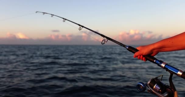 釣竿を持って魚を捕まえようとする女性の手 夕暮れ時に小さな波で船に乗りながら釣りを楽しむ女性 — ストック動画