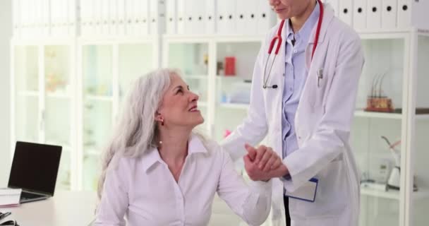 Hymyilevä Hoitava Lääkäri Auttaa Onnellisia Vanhuksia Isoäiti Seisomaan Klinikalla Auttaa — kuvapankkivideo