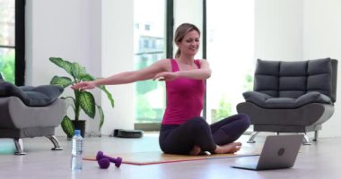 Genç fitness eğitmeni, video yoga dersi veriyor, konferans modunda dizüstü bilgisayarın önünde gerinme egzersizleri gösteriyor. Motivasyonlu kadın sanal spor eğitimine katılıyor