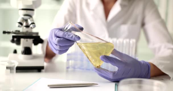 保護手袋の科学者の手は フラスコのクローズアップで黄色の液体を保持します 石油製品の分析 — ストック動画