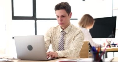Erkek öğrenci yöneticisi masada oturur dizüstü bilgisayara bakar ve yeni yazılım üzerinde çalışır. Stajyer görevleri tamamlar ve konsantrasyonla çalışır