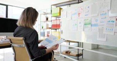 Kadın yönetici araştırma raporları üzerinde çalışıyor. Ofisteki beyaz tahtada istatistiksel bilgi kullanan pazarlamacı