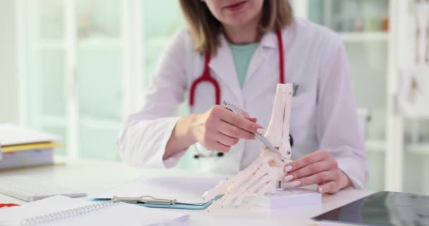 整形外科医は 診療所のテーブルの上に足の構造のモデルを示しています 人間の足の骨の解剖学と関節炎 — ストック動画