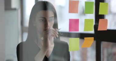 Cam duvardan bakan yaratıcı kadın notlar kullanır ve fikirleri paylaşır. Modern iş bürosu ve yaratıcı notlar