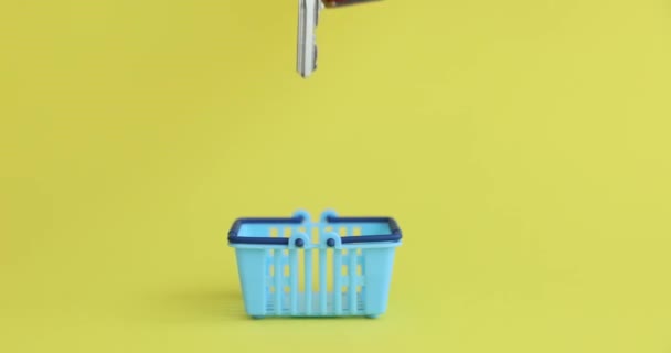 黄色い背景のクローズアップ4K映画の食料品のためのおもちゃのバスケットに家の鍵を入れて女性の手 物件概念の購入 — ストック動画