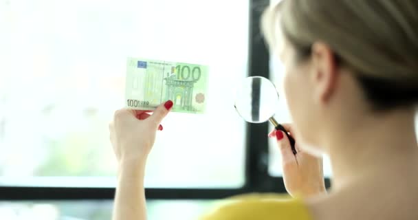女人透过放大镜看100欧元的钞票 并检查真人特写4K电影慢镜头 伪造货币概念 — 图库视频影像