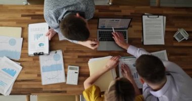Çalışkan iş arkadaşları, ofisteki ahşap masada oturan bilgisayardaki grafiklerden bilgileri inceliyor. Takım çalışması kavramı ve finansal proje sorunları tartışması