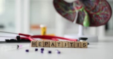 Karaciğer modeline ve hastane ofisindeki steteskopa karşı bloklardan oluşan Hepatit hastalığı. Dağınık haplar ve şırınga, tıp alanında uzmanlaşmış kişilerin masasında yatıyor.