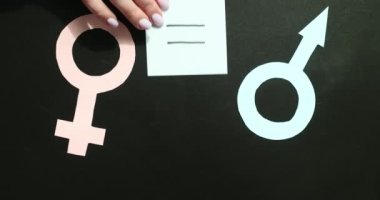 Kadın eli, siyah arka planda kadın ve erkek kağıt sembolleri arasına denklem işareti koyar. Çağdaş toplumda eşit haklar ve cinsiyet fırsatları