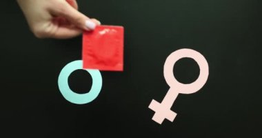 Kadın eli siyah arka planda erkek ve kadın sembollerine prezervatif paketi koyar. Cinsel yolla bulaşan hastalıklardan korunma. İstenmeyen hamileliğin önlenmesi