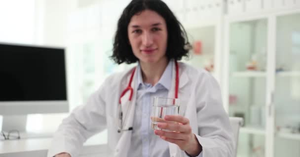 慎重な男性医師は喉の渇き患者に水のガラスを与えます 若い専門家は病院で病人の世話をする 現代の診療所での医療 — ストック動画