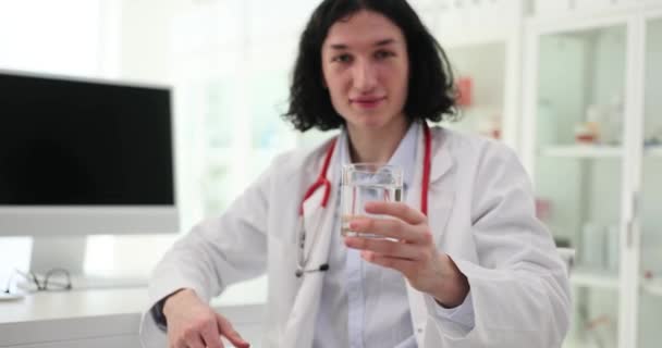 Smilende Mandlige Læge Med Langt Hår Tilbyder Glas Mineralvand Til – Stock-video