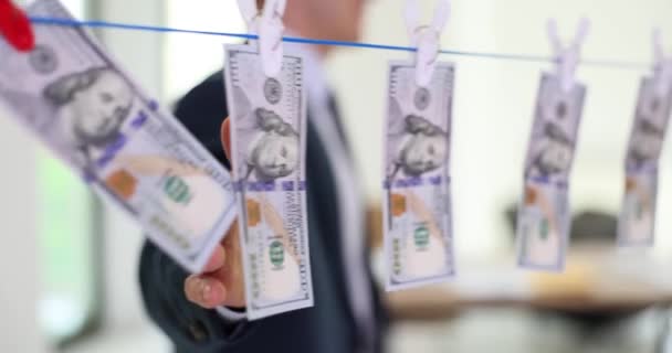 年轻的商人摸着湿透了的美元钞票 挂在用别针固定的晾衣绳上晾干 人类隐藏非法获得的钱的来源 — 图库视频影像