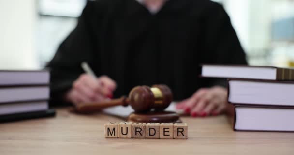 砂利の近くのテーブルでノートを作る裁判官に対して木製のキューブで作られた言葉の殺人 裁判所の労働者は裁判所で重大な犯罪の判決を下し — ストック動画