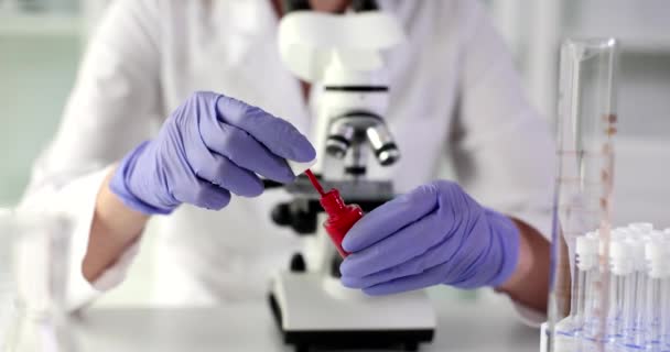 戴橡胶手套的科学家在电子显微镜下打开红色指甲油 化验室工作人员准备检查化妆品慢动作 — 图库视频影像