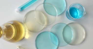 Masada renkli bir sıvı bulunan profesyonel bir laboratuvar bardağı. Test tüplü cam şişe ve sarı ve mavi reaksiyonlu Petri kabı.