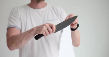 Adam ışık stüdyosunda kağıt levhayı keskin bıçakla keser. İnsan, beyaz arka planda et kesmek için mutfak çatal bıçak takımının kalitesini inceliyor.