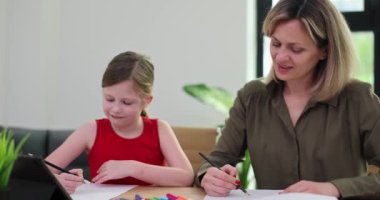 Pozitif kadın küçük kıza tablet kullanarak ödevlerini yapmasına yardım ediyor. Öğretmen, okul kızına oturma odasında ağır çekimde anlatılan şeyleri anlatıyor.