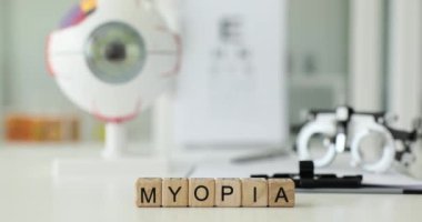 Tahta bloklardan gelen Myopia 'ya karşı hastane ofisindeki beyaz masada duran gözlük ve göz modelleri. Oftalmolojik tanı araçları konsepti