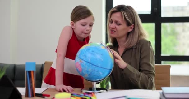 好奇心旺盛な少女と前向きな女性は机の上で地球を見る 学生は自宅で母親と世界地図を探索します 地理学の授業スローモーション — ストック動画