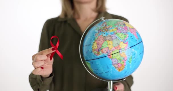 女性は赤いリボンと地球をライトスタジオで持っています 国際エイズ啓発デー 女性は世界中のHiv陽性患者への支援を示しています — ストック動画