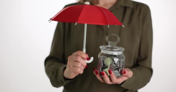 女人用红色雨伞把钱罐盖在白色背景上 资金储蓄保险 保护货币资产概念 — 图库视频影像