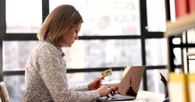 Odaklanmış bir kadın, ofiste oturan bir dizüstü bilgisayarla kredi kartı bilgilerine ulaşır. Müdür yavaş çekimde online ödeme yapıyor