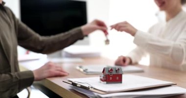 Emlakçı, yeni yazlık evin anahtarını kadın müşteriye veriyor. Kadınlar ofiste yavaş çekimde başarılı bir anlaşma yaptıktan sonra el sıkışırlar.