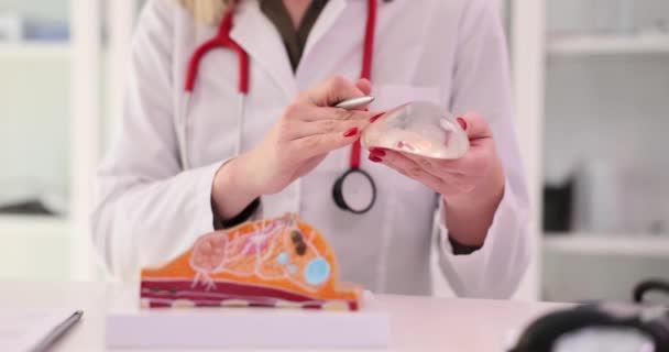医学专业的女性专家将笔尖指向人工乳房持有硅酮植入物模型 妇女在医院慢动作解释工作场所的女性疾病 — 图库视频影像