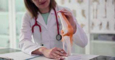Kadın doktor, klinik önermelerinde ışık masasında oturan iskelet modelinin diz eklemini açıklıyor. Stajyerler için ağır çekimde danışmanlık