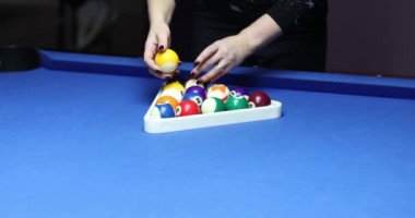 Bir kadın mavi bilardo masasındaki üçgen rafa renkli toplar koyar. Kadın spor kulübünde oyun için ekipman hazırlıyor. Boş zaman eğlence konsepti yavaş çekim