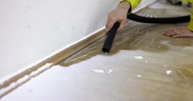İşçi, elektrik süpürgesiyle zemini tozdan temizliyor. Erkek uzman, ağır çekimde duvarları ovalayarak toprağı temizliyor.