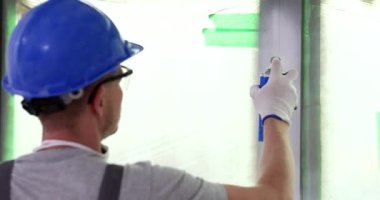 Üniformalı bir erkek, dairesinde sprey boya ile pencere çerçevesini boyuyor. Ressam iç unsurlara renk uygular. Oda yenileme konsepti yavaş çekim